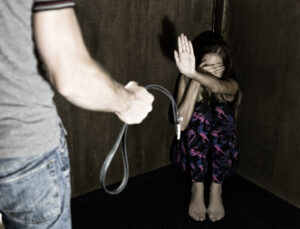 frightened woman sitting in the corner with a faceless man holding a belt, a conceptual shoot portraying the process and effects of domestic violence.